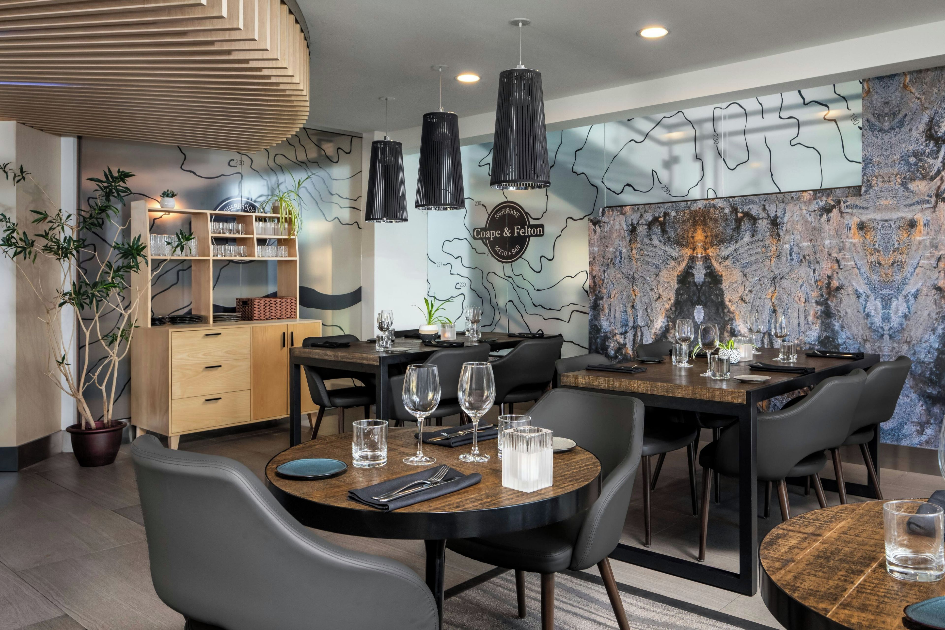 A modern dining area with a wooden table, black chairs, and a marble wall with a map design.