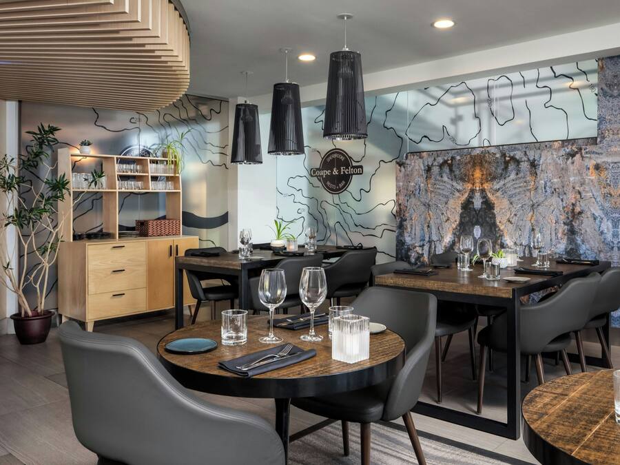 A modern dining area with a wooden table, black chairs, and a marble wall with a map design.