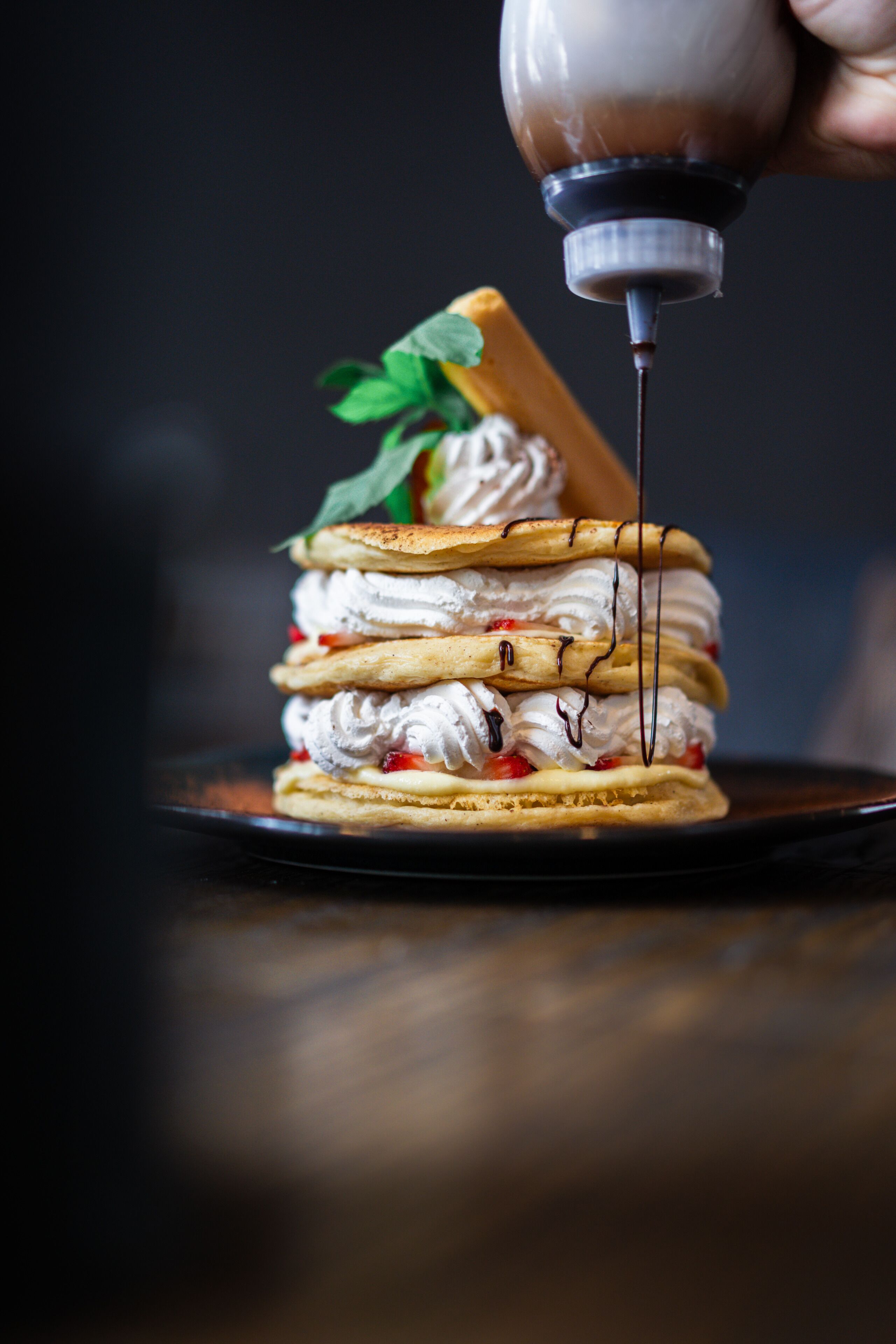 A dessert with whipped cream and chocolate sauce being poured over it.