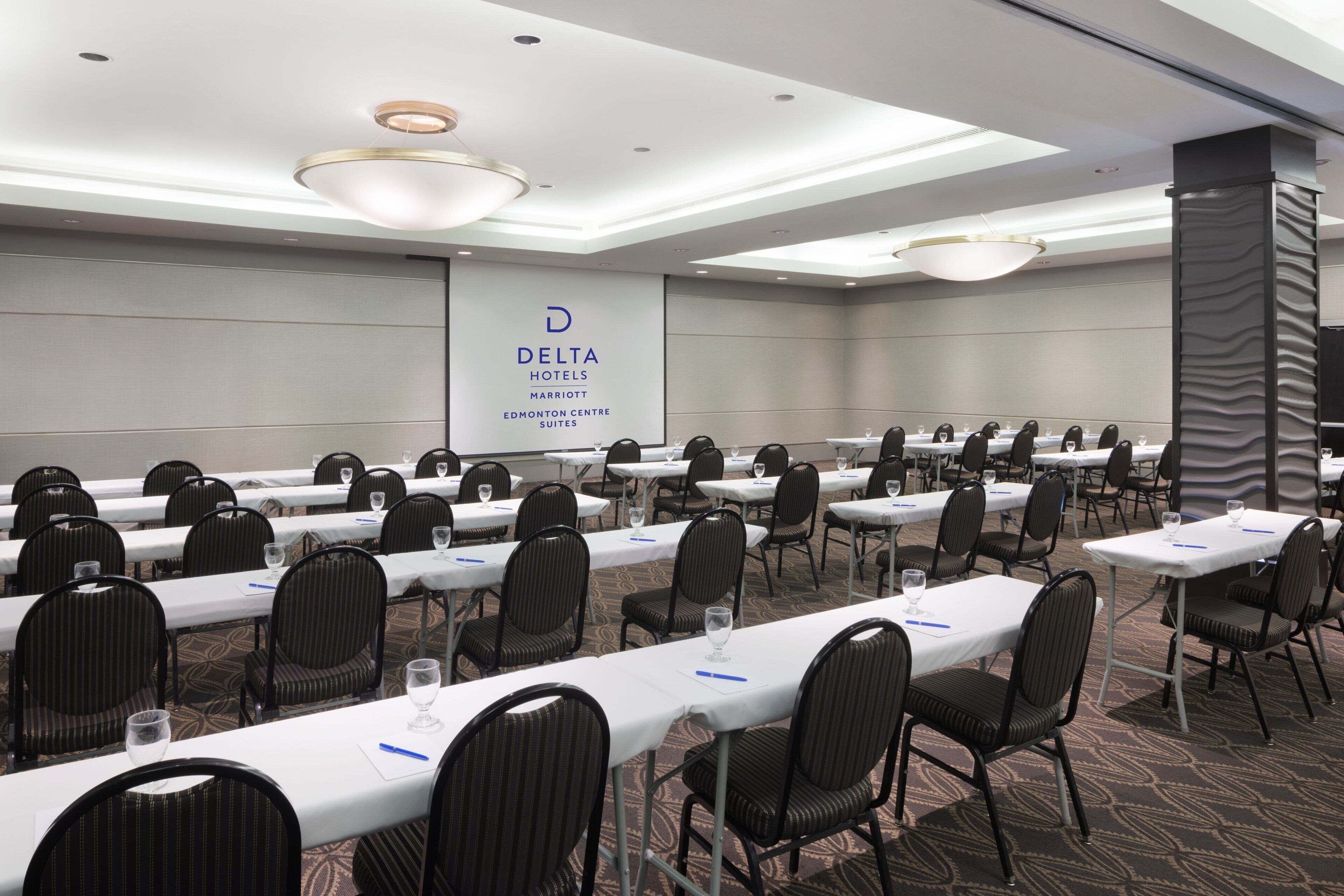 A conference room with rows of tables and chairs, a large banner with the Delta Hotels logo, and a patterned carpet.