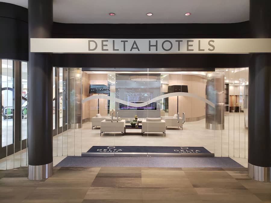 La entrada de un Hotel Delta con una decoración moderna, incluyendo una zona de recepción con asientos y una pantalla grande.
