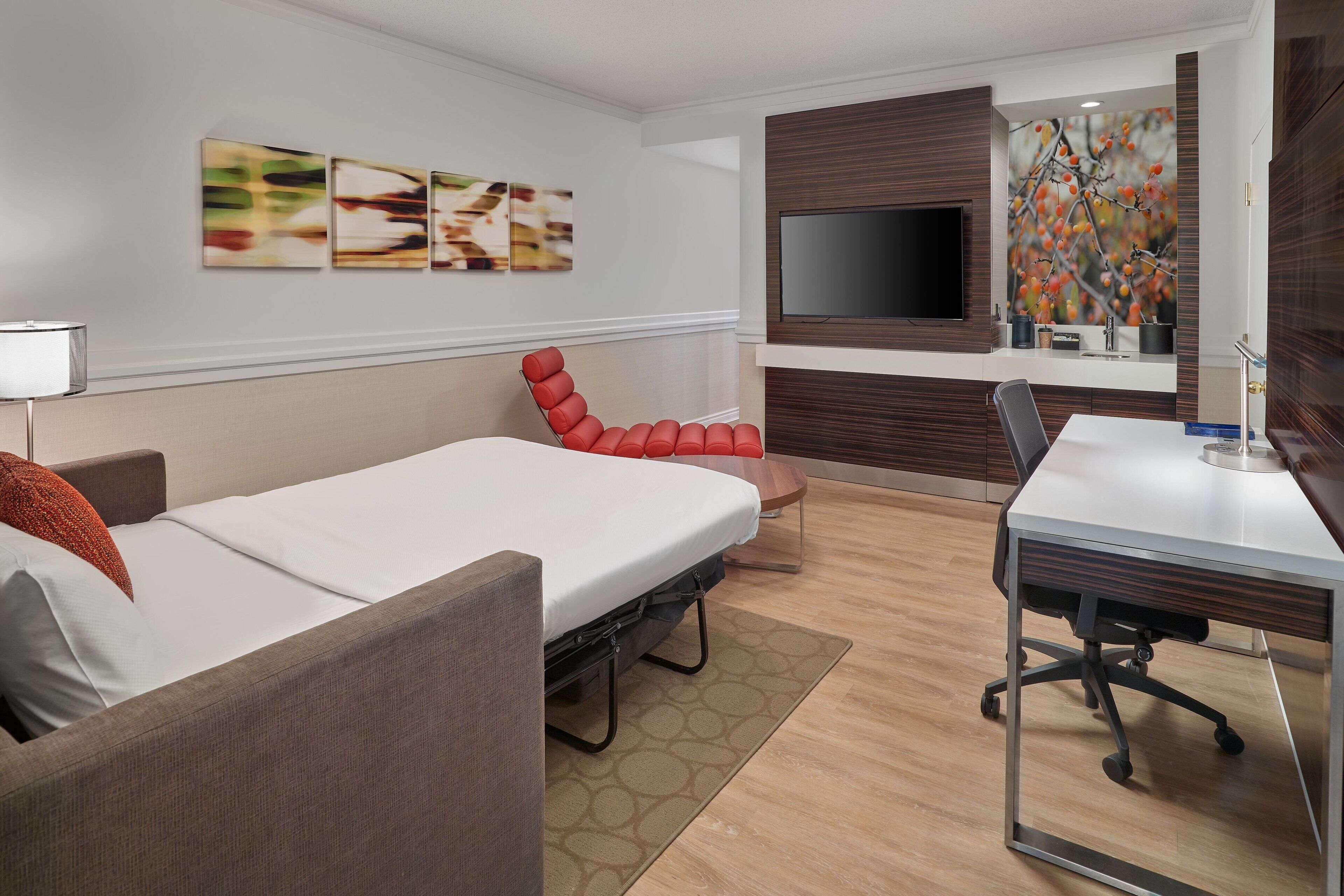 Une chambre d’hôtel moderne équipée d’un lit, d’un bureau, d’une chaise, d’un téléviseur et décorée avec des œuvres d’art abstraites sur les murs.