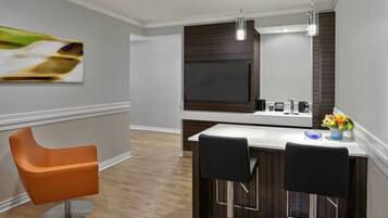 A modern kitchen with a large TV, two bar stools, and a bar counter.