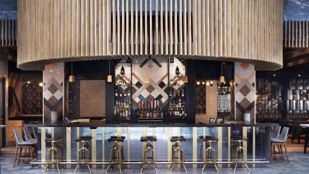 Eine Bar mit einer zentralen Theke, mehreren Barhocker und hängenden Pendelleuchten.