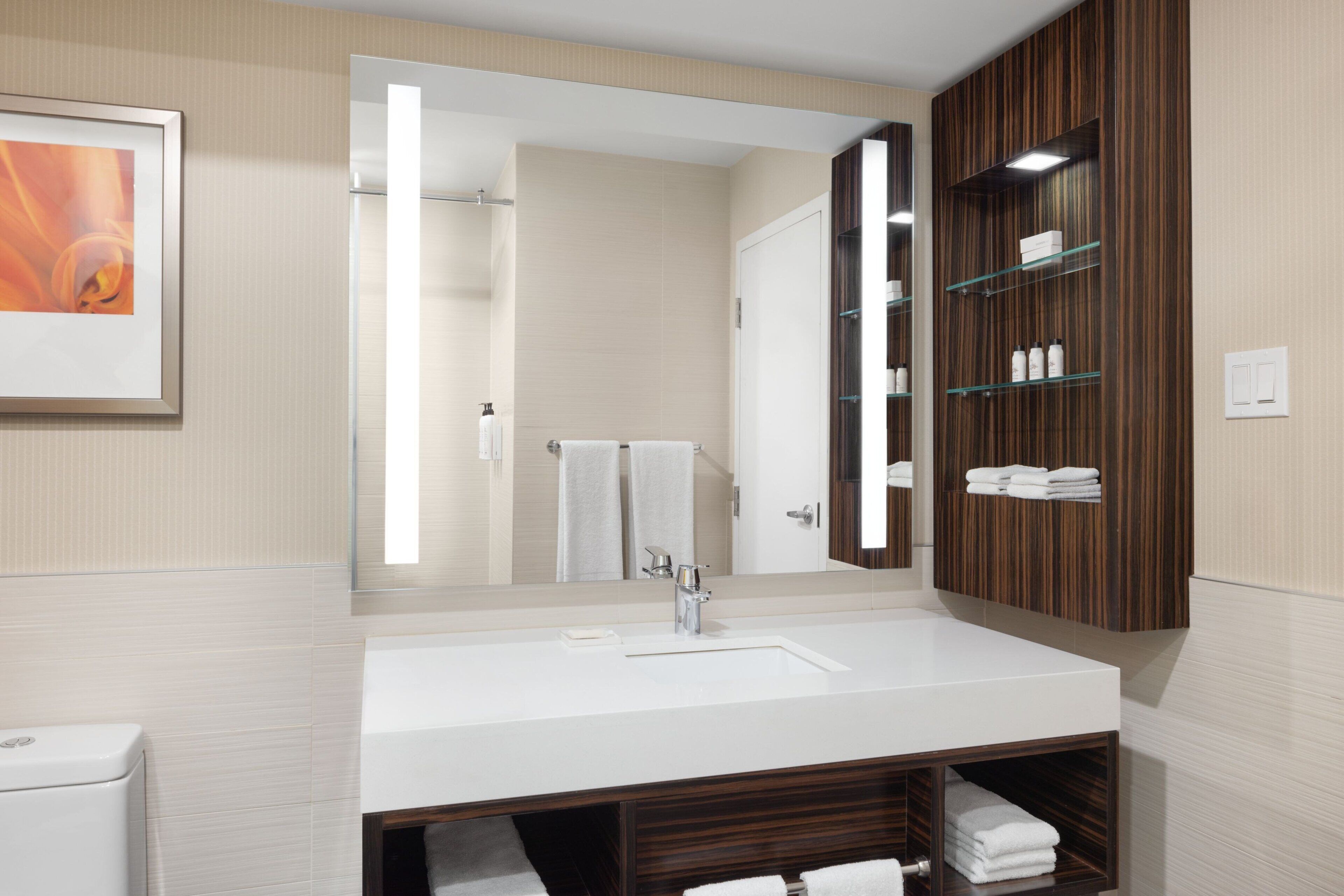 Un baño moderno con un espejo grande, lavamanos blanco y tocador de madera.