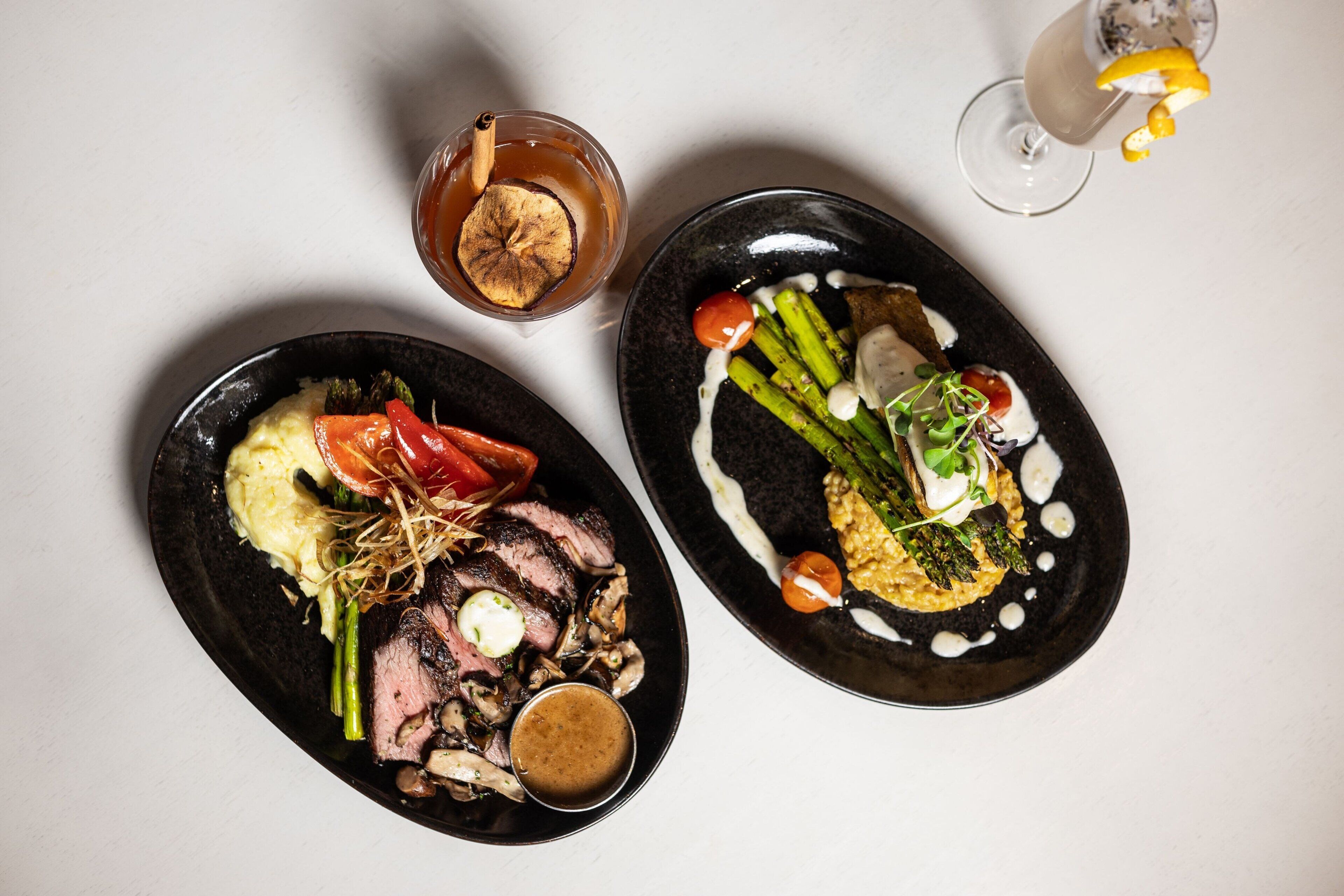 Two plates of food with a glass of drink and a bowl of sauce.