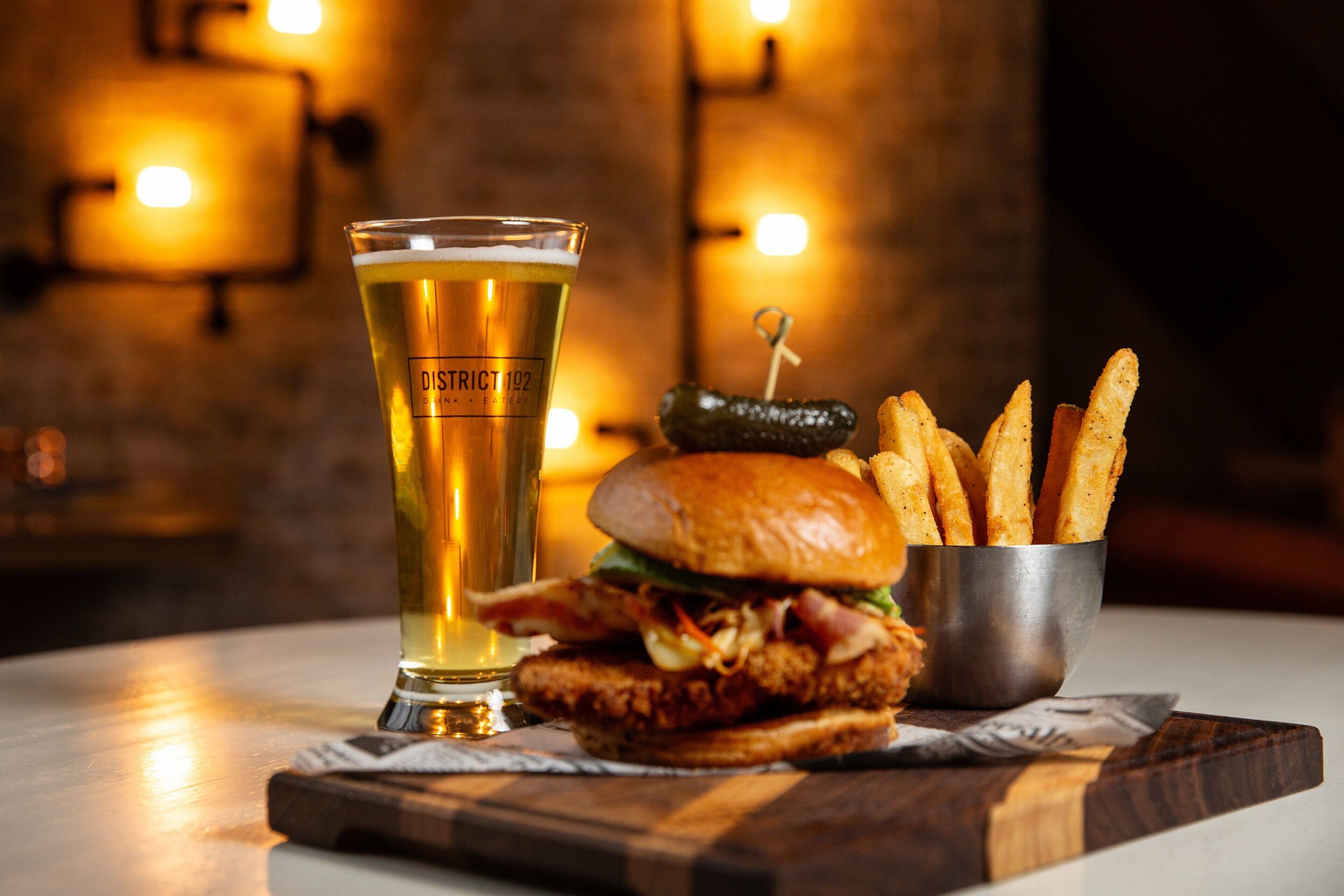 A meal consisting of a burger, fries, and a glass of beer on a wooden table.