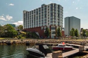 A waterfront hotel with a dock, a boat, and a cityscape in the background.