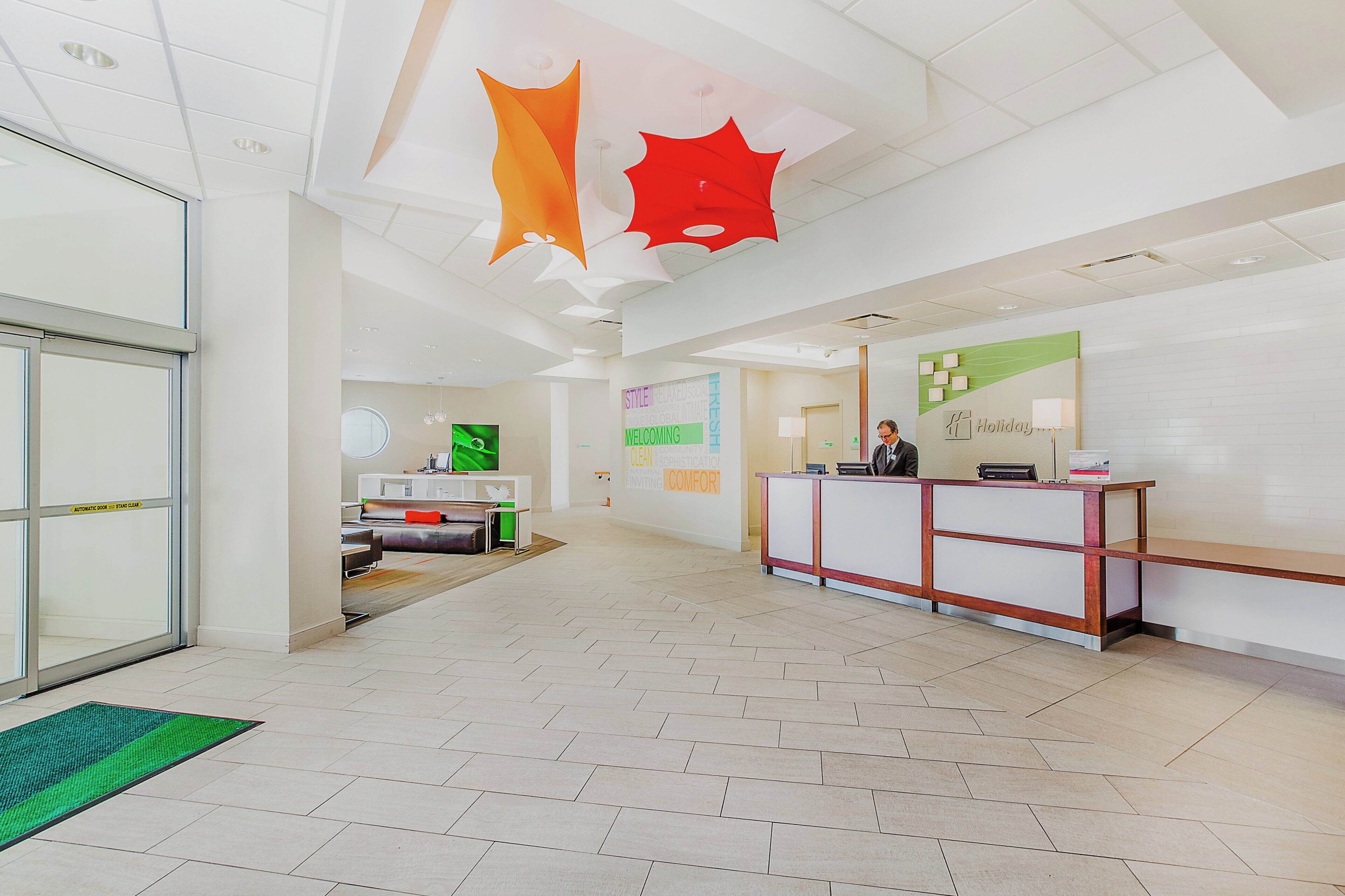 A hotel reception area with a reception desk, a seating area with a sofa, and a wall with a welcome sign.