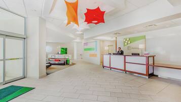 A hotel reception area with a reception desk, a seating area with a sofa, and a wall with a welcome sign.