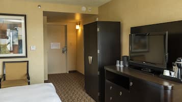 A hotel room with a bed, a TV, a minibar, and a door leading to a hallway.