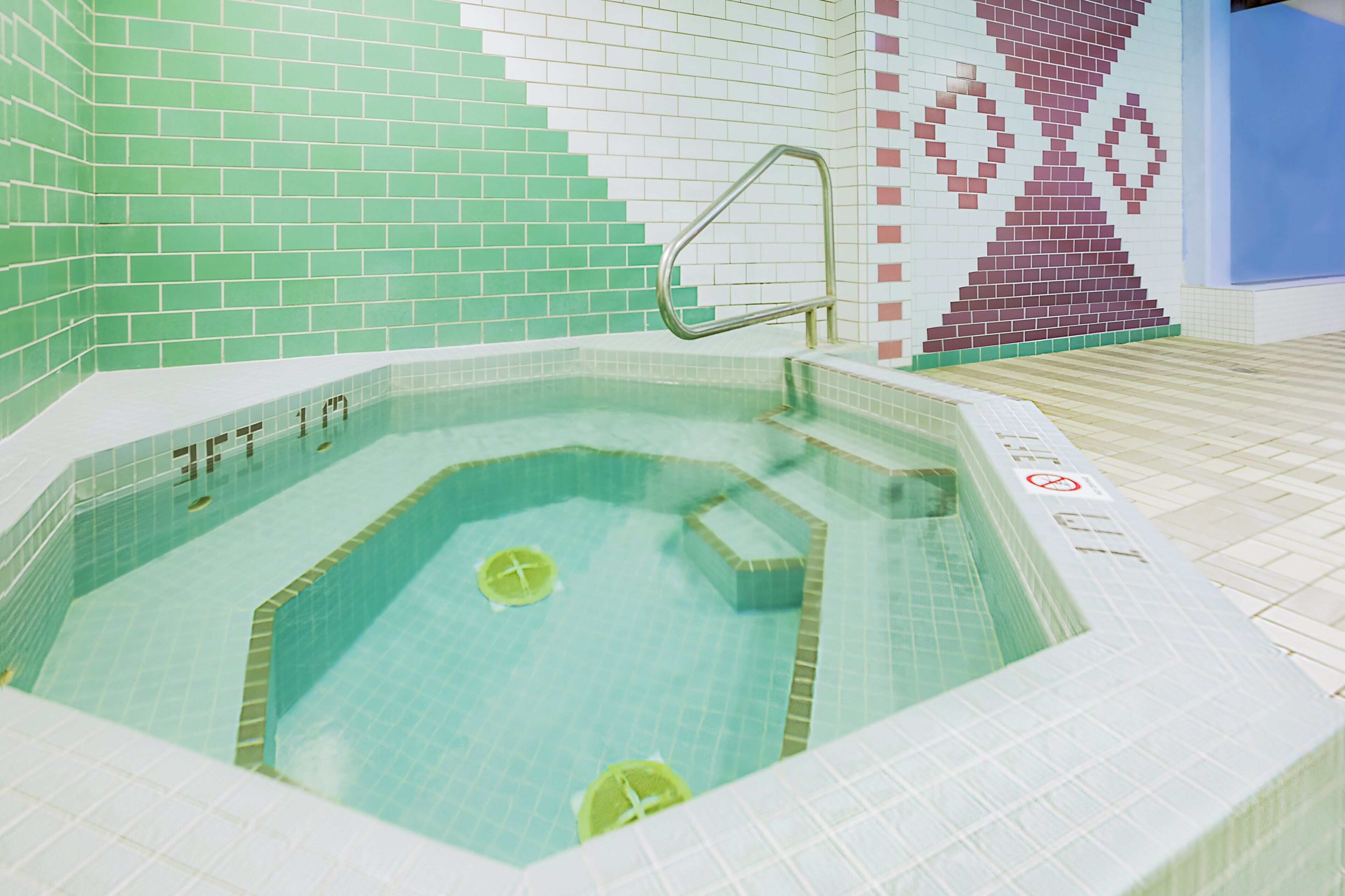 Un jacuzzi con interior de azulejos, una escalera metálica y un letrero de 'prohibido el paso' en el suelo.