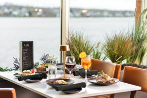 A dining table set with plates, glasses, and a menu, overlooking a body of water. - Holiday Inn Sydney - Waterfront by IHG (Sydney)