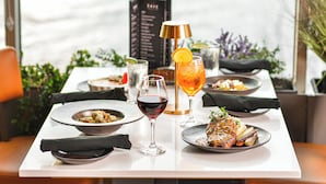 A dining table with plates of food, a glass of red wine, and a cocktail with an orange slice garnish. - Holiday Inn Sydney - Waterfront by IHG (Sydney)