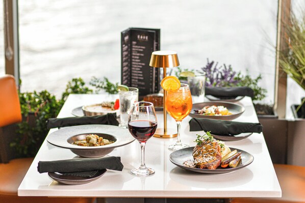 A dining table with plates of food, a glass of red wine, and a cocktail with an orange slice garnish.