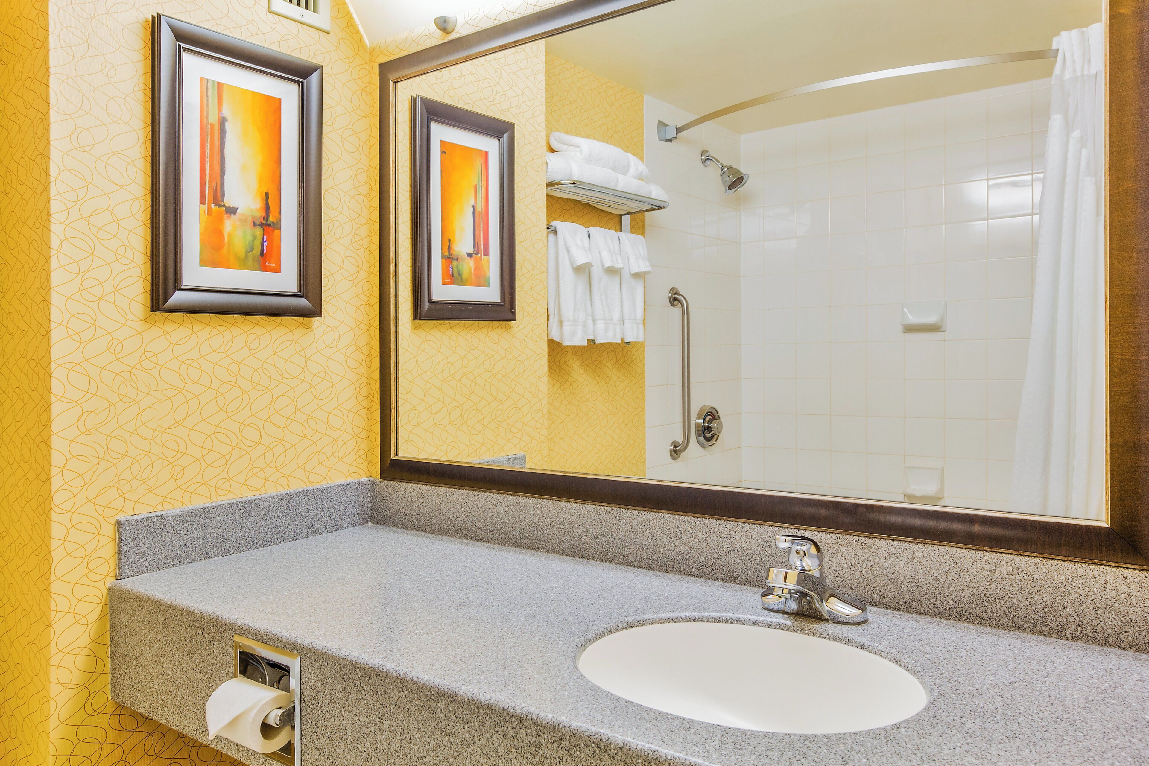 Ein Badezimmer mit einer Arbeitsplatte aus Granit, einem Waschbecken, einem Spiegel und einer Dusche mit Glastür.