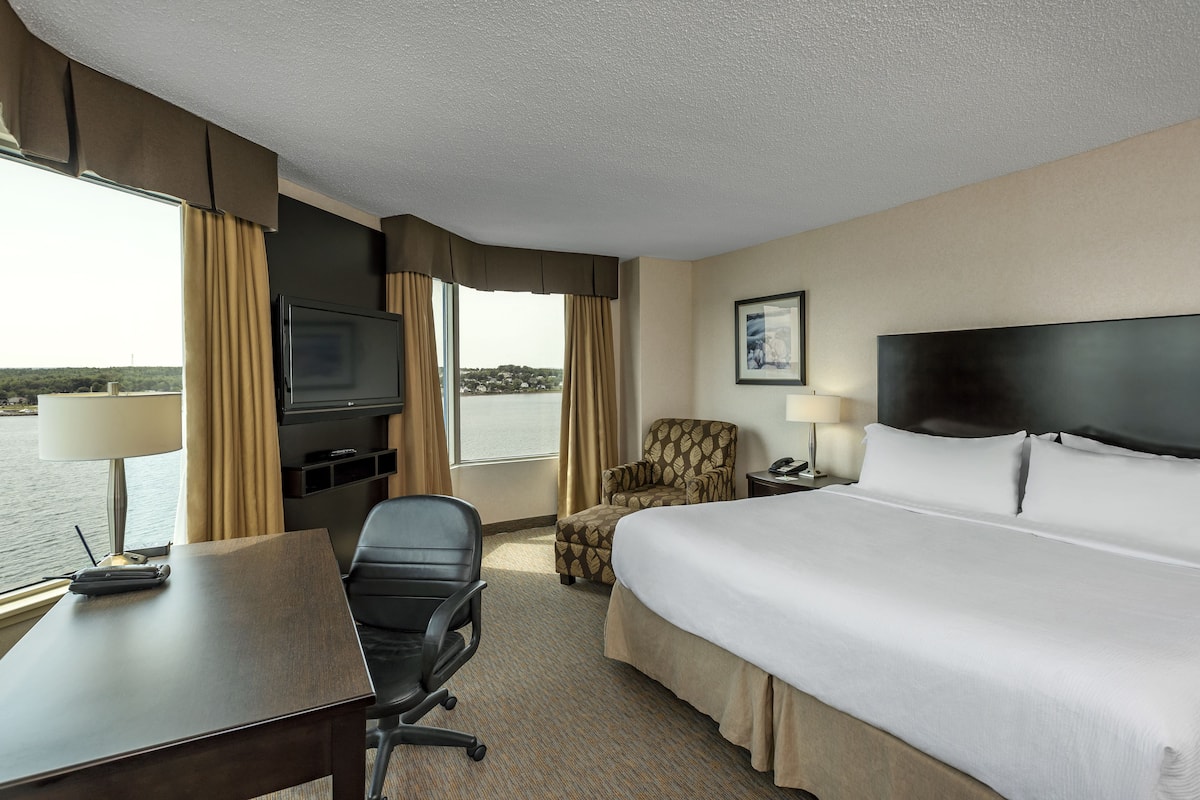 A hotel room with a bed, desk, chair, TV, and a view of the water.