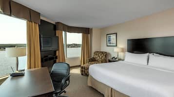 A hotel room with a bed, desk, chair, television, and a view of the outdoors.