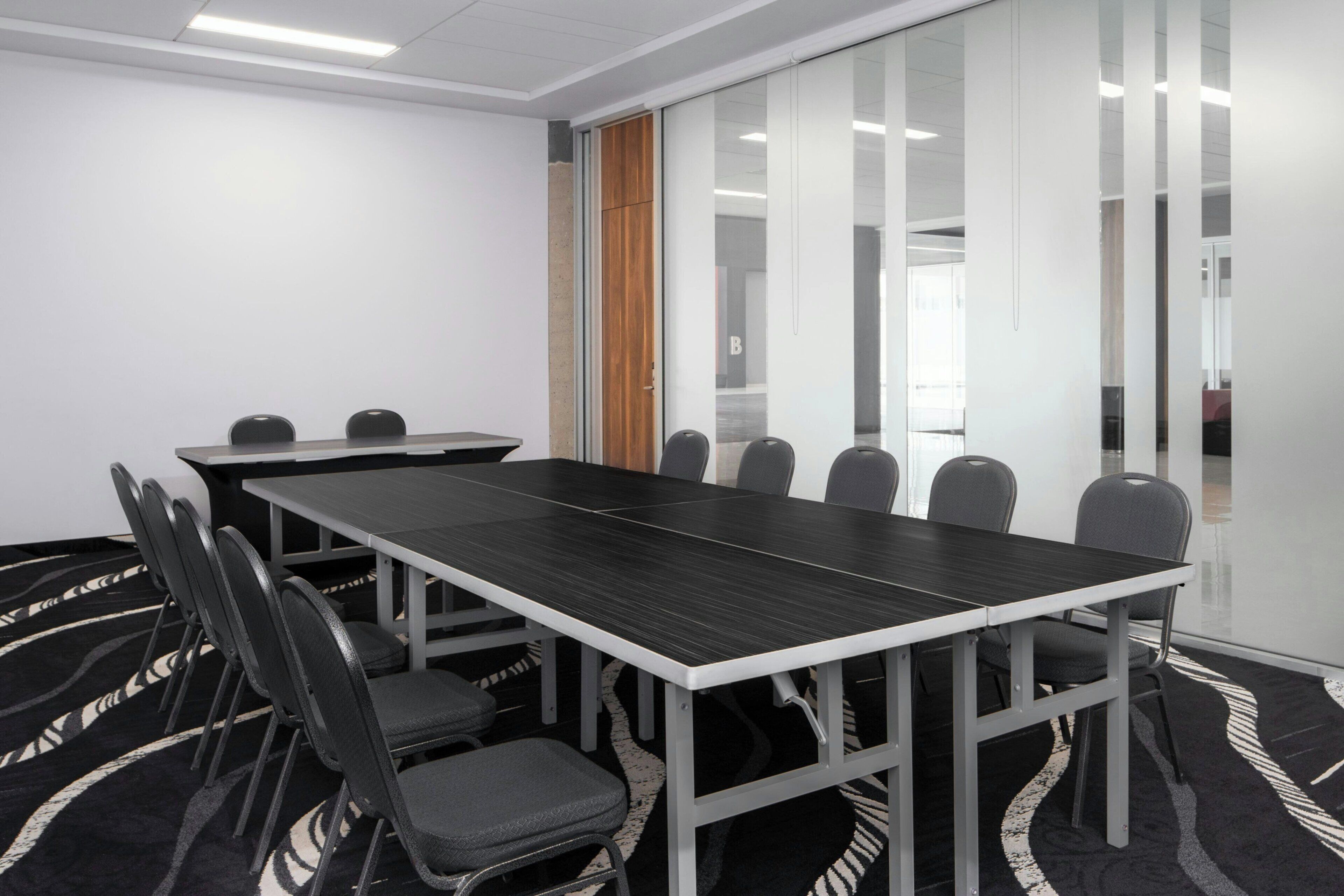 A conference room with a long table, chairs, and a patterned carpet.