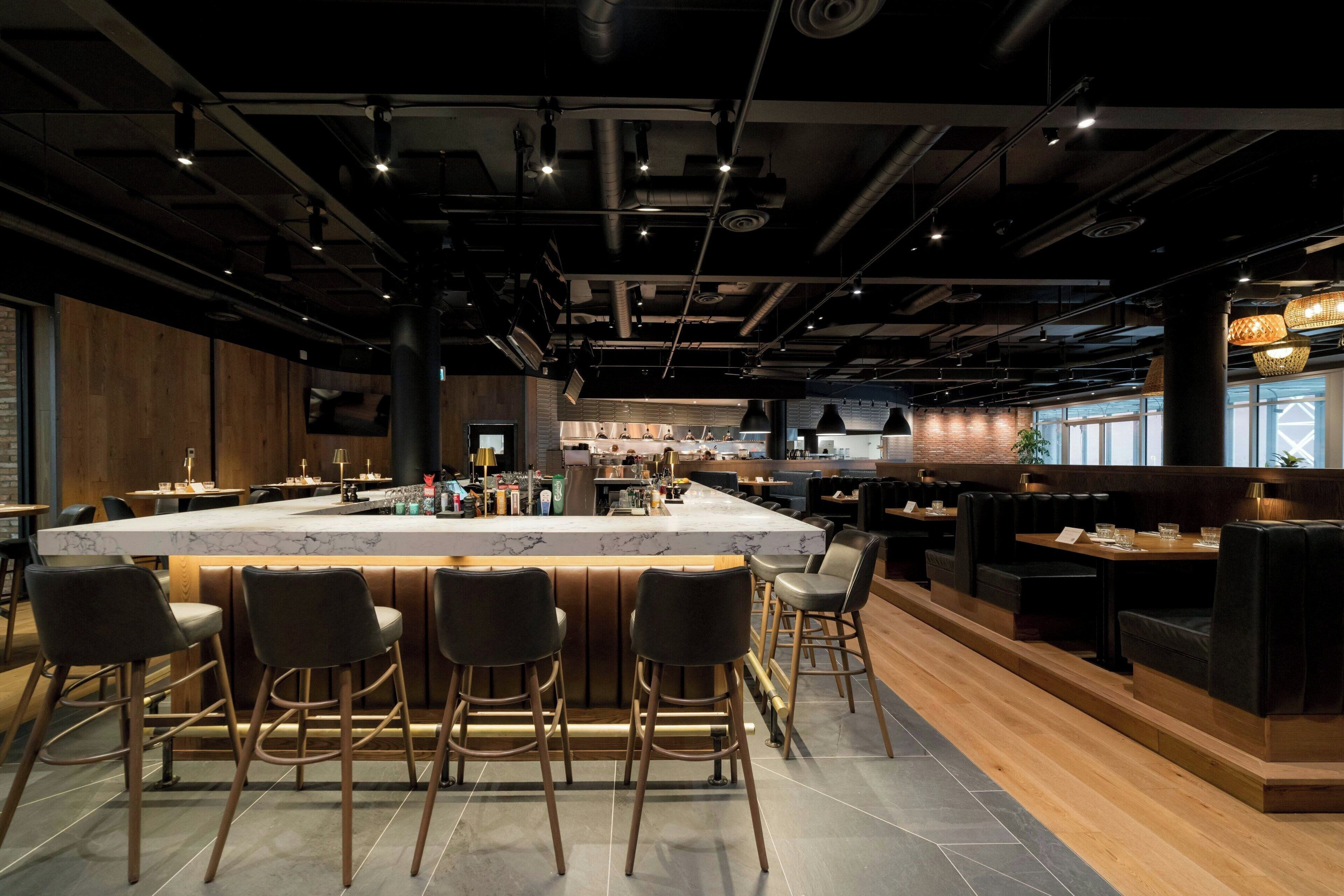 A modern bar area with a marble countertop and bar stools, surrounded by wooden accents and seating.