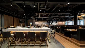 A modern bar area with a marble countertop and bar stools, surrounded by wooden accents and seating.