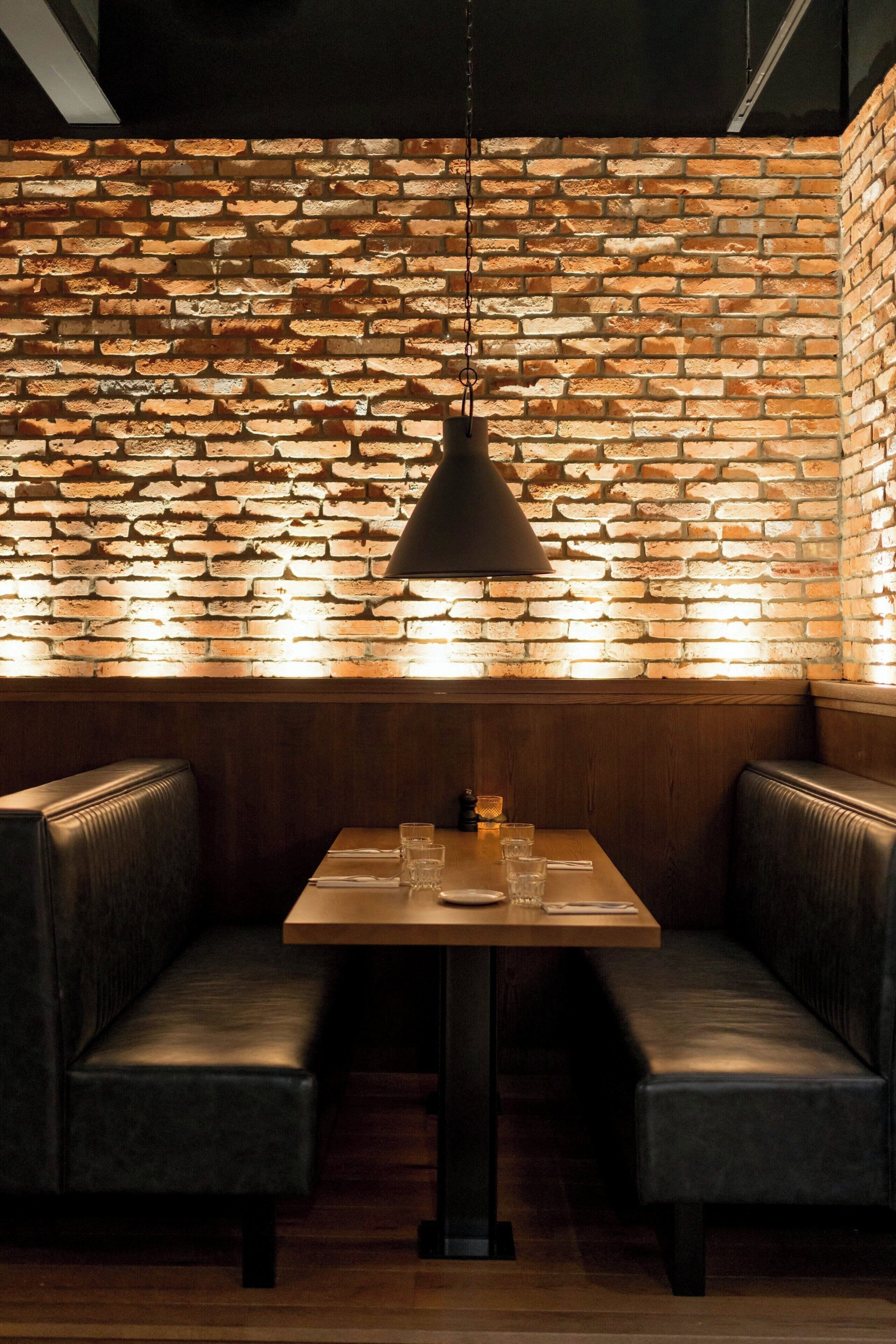 A restaurant with a brick wall, wooden table, and leather booths.