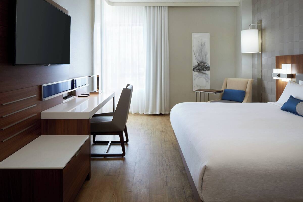 Une chambre d’hôtel avec un lit, un bureau, une chaise, une télévision et un tableau au mur.