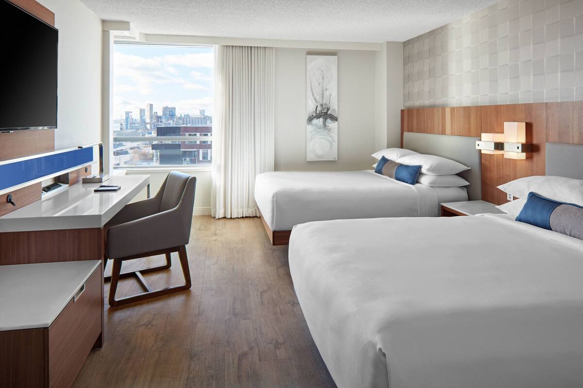 Une chambre d’hôtel équipée d’un bureau, de deux lits, d’une télévision et offrant une vue sur la ville.