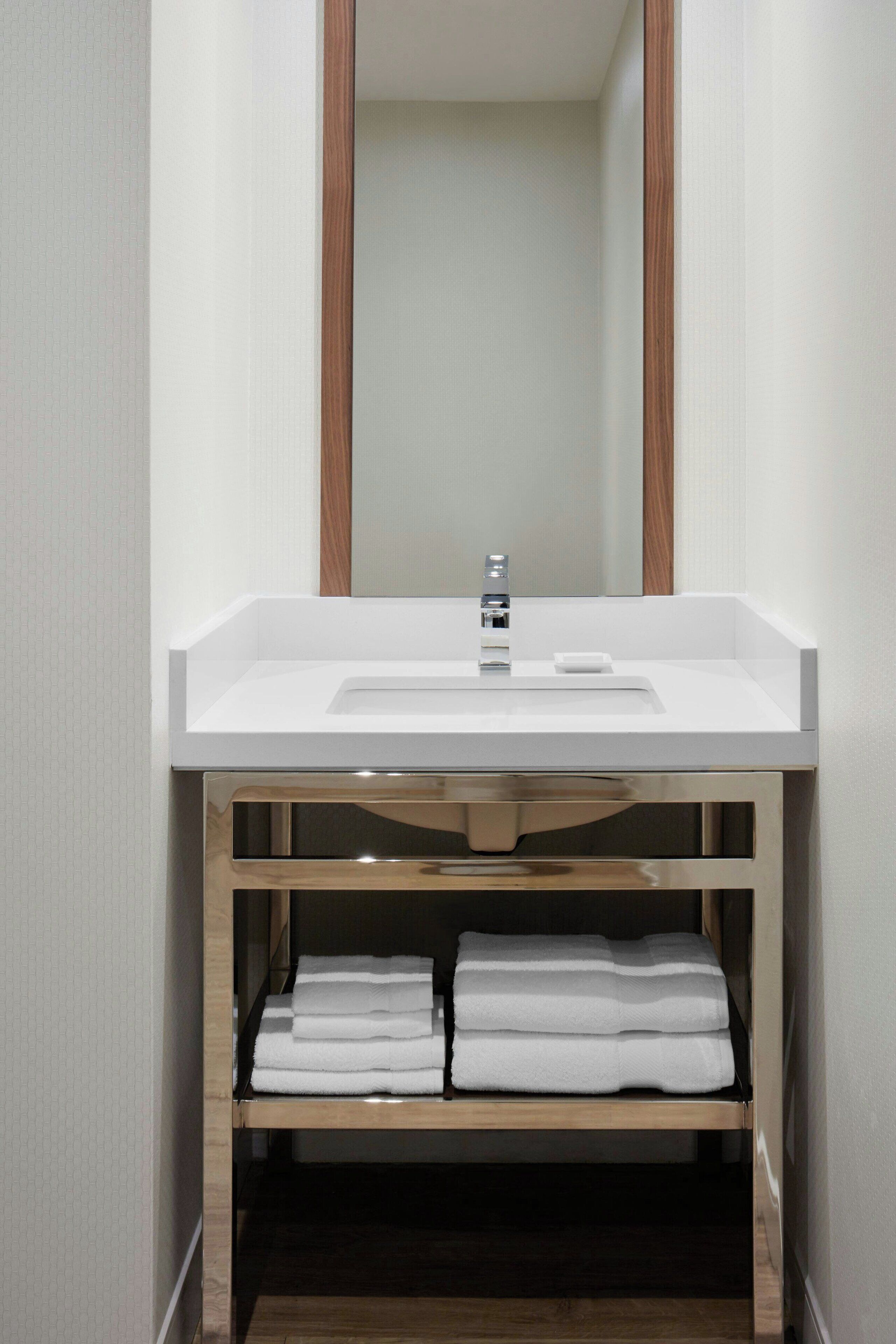 A bathroom with a white sink, a mirror, and a shelf with folded towels.