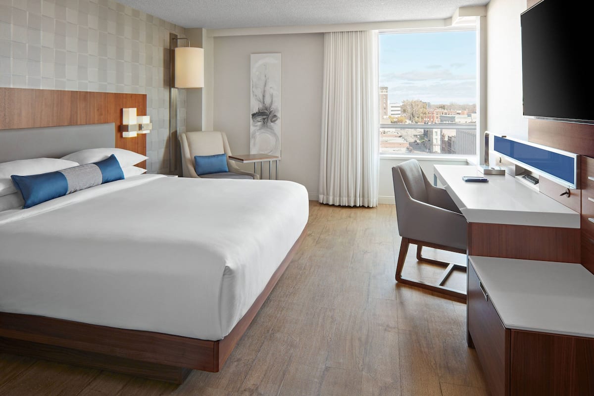 Une chambre d’hôtel avec un grand lit, un bureau avec un ordinateur, une chaise et une vue sur la ville par la fenêtre.