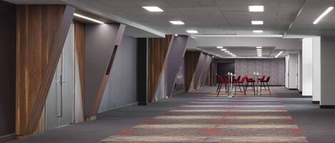 A long, narrow hallway with a patterned carpet, wooden paneling on the walls, and a row of red chairs at the end.