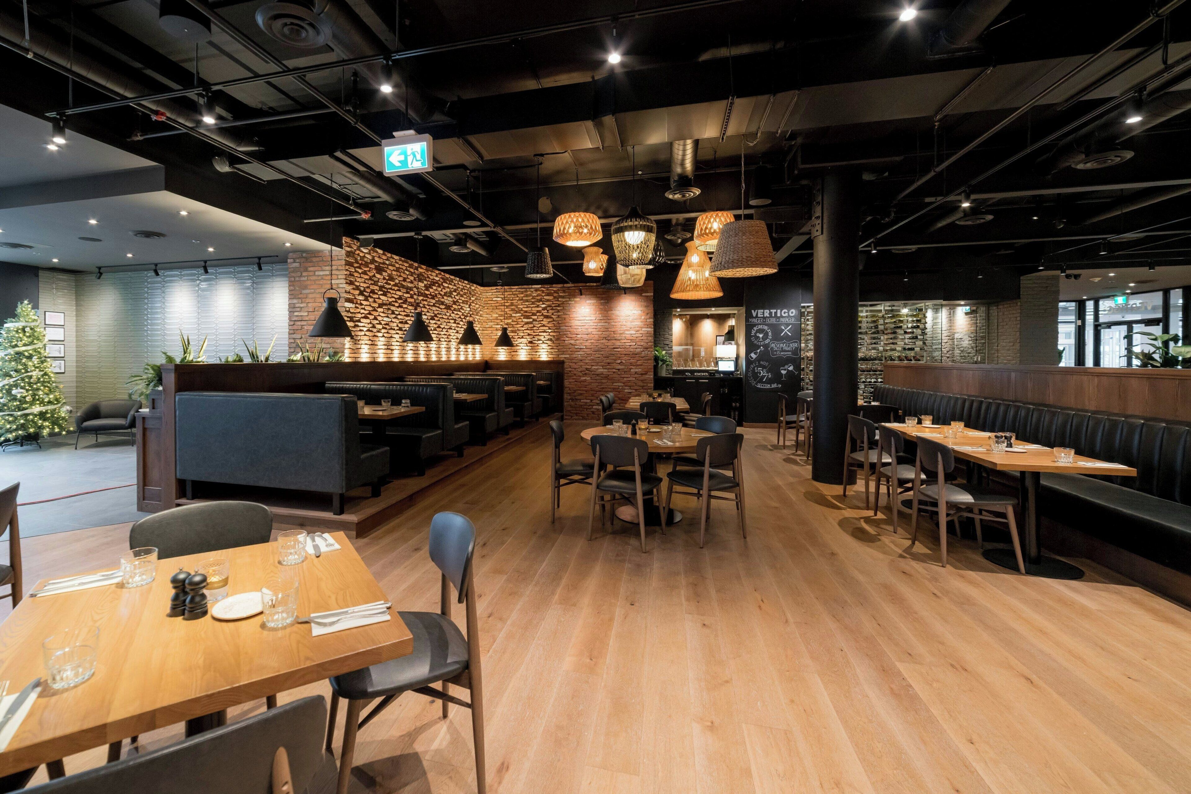 A modern restaurant interior with wooden flooring, black and wooden furniture, and hanging pendant lights.