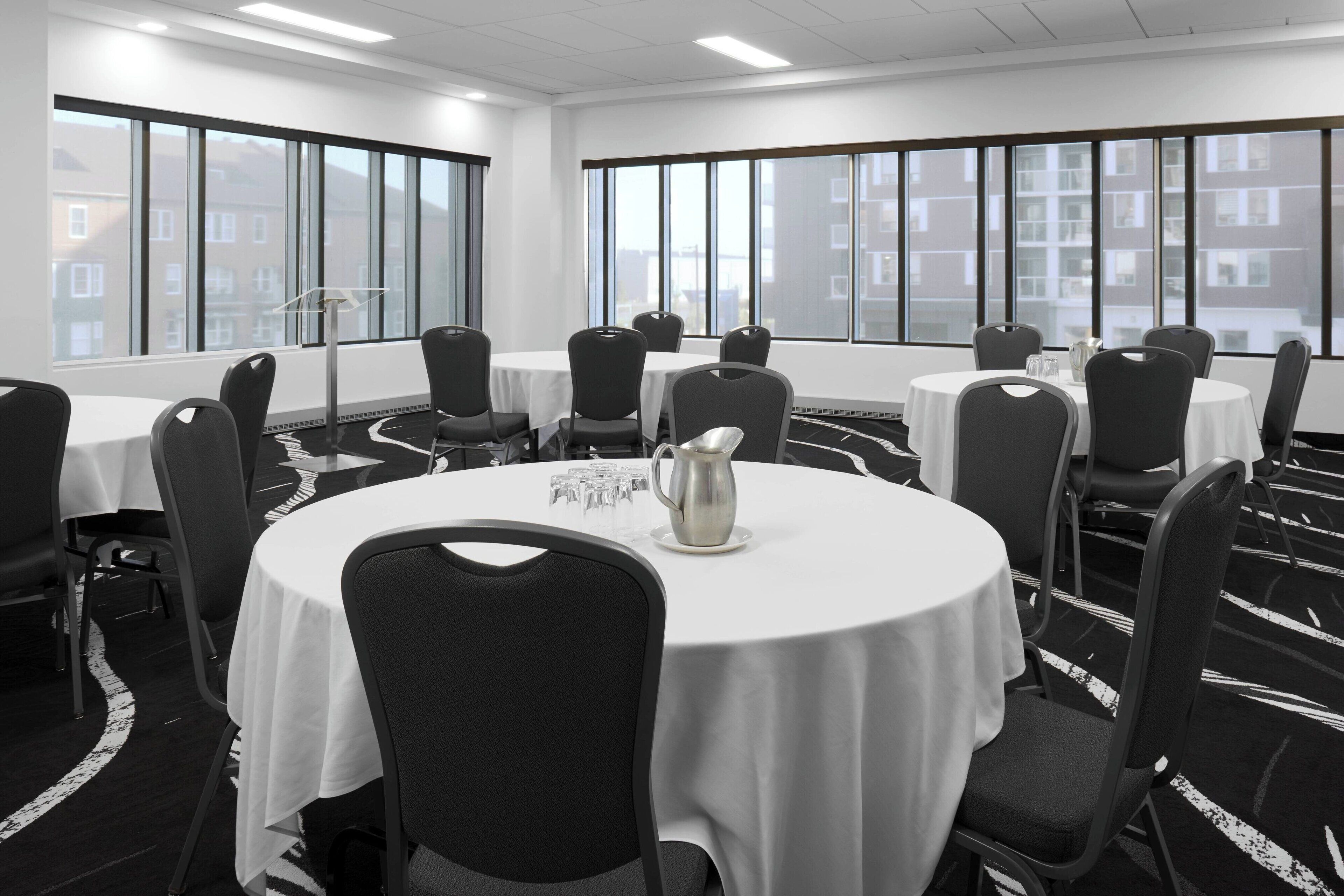 A conference room with round tables, black chairs, and a white tablecloth.