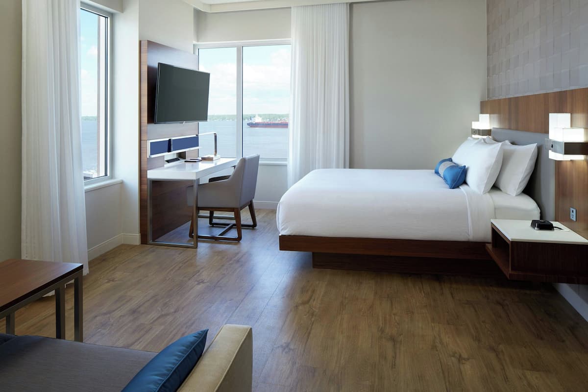 Une chambre d’hôtel équipée d’un lit, d’un bureau, d’une télévision et de grandes fenêtres donnant sur la mer.