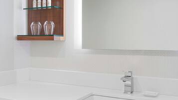Un baño moderno con un lavamanos blanco, un espejo grande y un mueble de tocador de madera con estantes de vidrio.