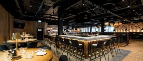Un restaurante moderno con barra central, techo alto con conductos expuestos y una combinación de taburetes de bar y sillas de comedor.