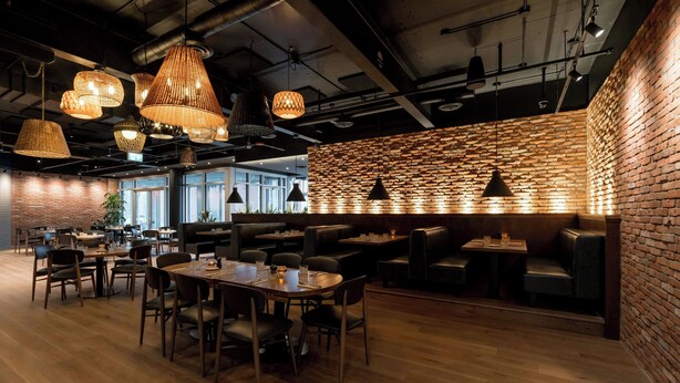 A modern restaurant with wooden tables and chairs, hanging wicker lamps, and a brick wall. - Delta Hotels by Marriott Trois Rivieres Conference Centre (Trois-Rivieres)