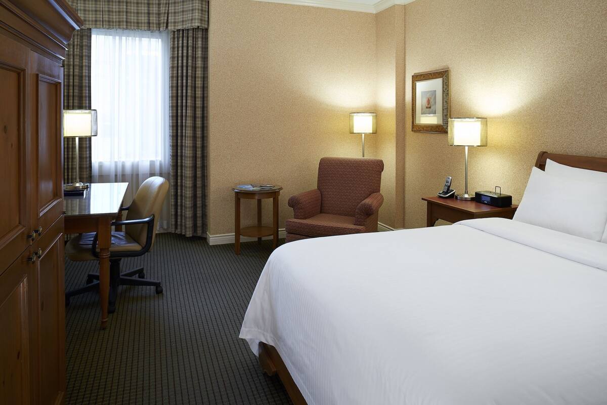 A hotel room with a bed, a desk, a chair, and two bedside lamps.