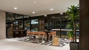 Un espacio interior moderno con una pared de vidrio, una zona de comedor con sillas y una mesa, y una planta en maceta.