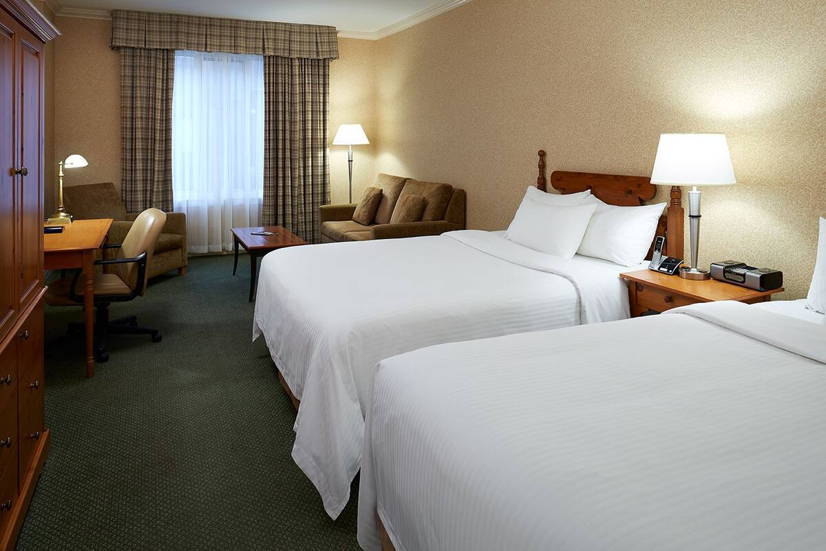 A hotel room with two beds, a desk, a chair, a lamp, and a wardrobe.