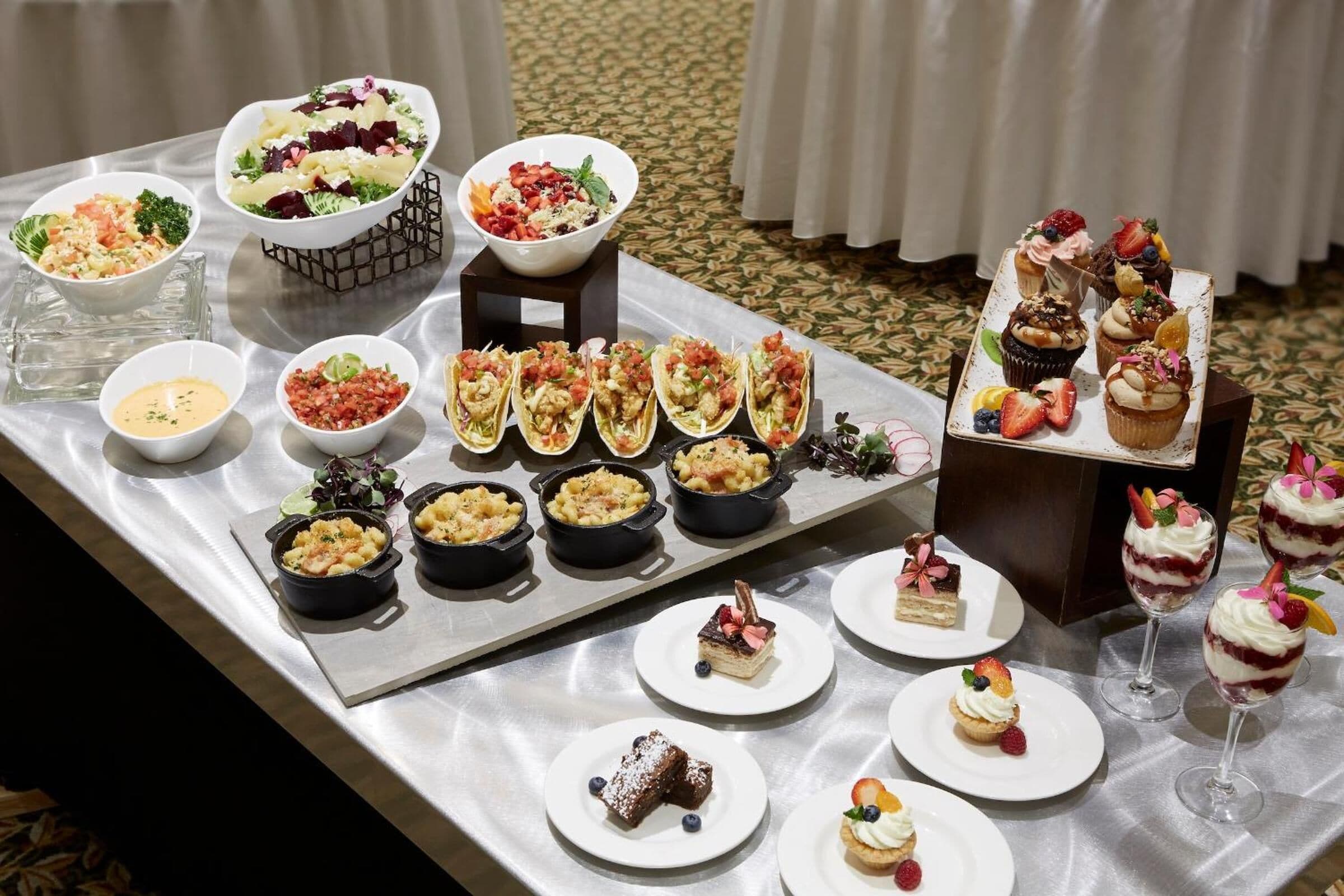 Una mesa de buffet con diversos platos, entre ellos ensaladas, postres y aperitivos.