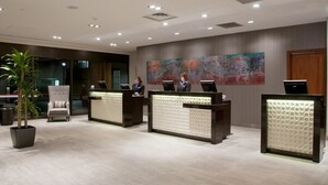 Zona de recepción de hotel con tres mostradores, un cuadro abstracto grande en la pared y una planta en maceta.