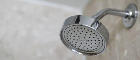 Un pommeau de douche chromé, de forme circulaire et orné du logo Kohler, fixé sur un mur dont la surface est recouverte de carreaux.