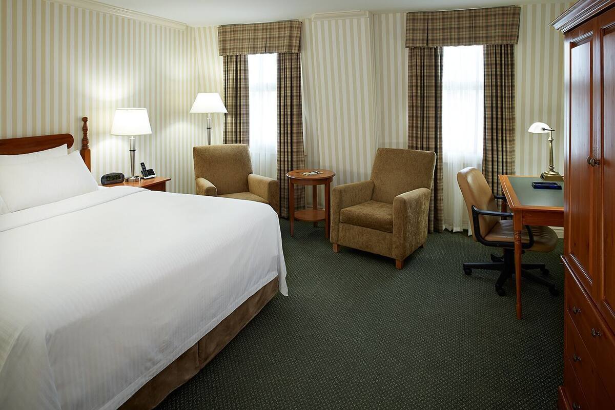 A hotel room with a large bed, two armchairs, a desk, and a dresser.
