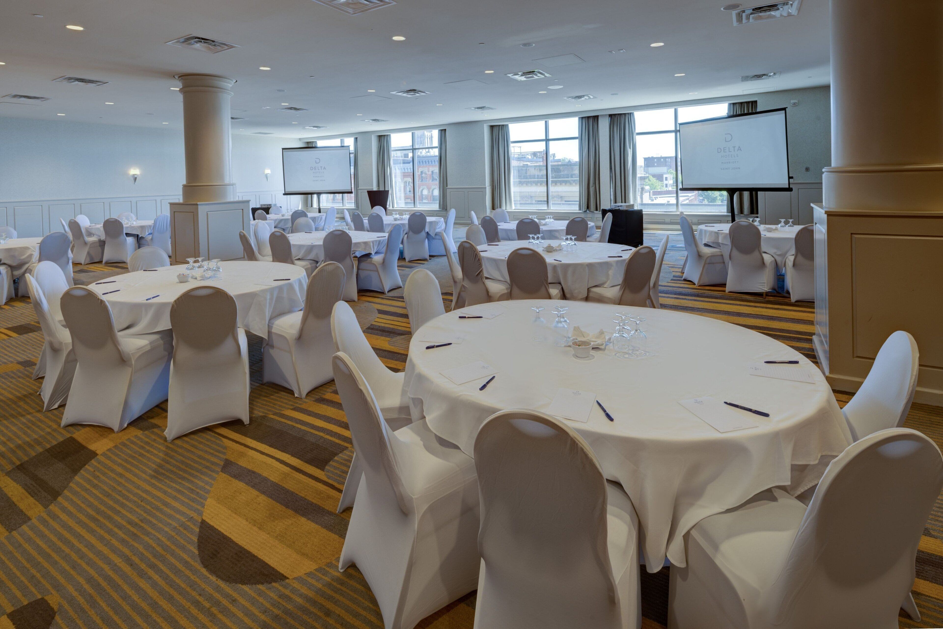 Une salle de conférence équipée de plusieurs tables rondes, de chaises blanches et d’un grand écran pour les présentations.