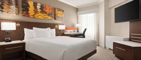 A hotel room with a large bed, bedside tables, a desk with a chair, a flat-screen TV, and artwork on the wall.
