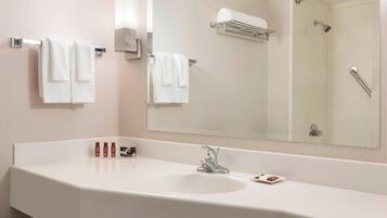 A hotel bathroom with a white sink, two towels hanging on towel bars, a mirror, and a shower area.