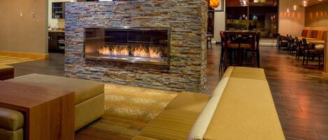 Un área de descanso moderna con chimenea de piedra, asientos cómodos y un comedor con mesas y sillas.