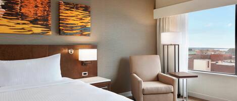Habitación de hotel con una cama grande, una silla, una mesita pequeña y dos lámparas fijadas a la pared.