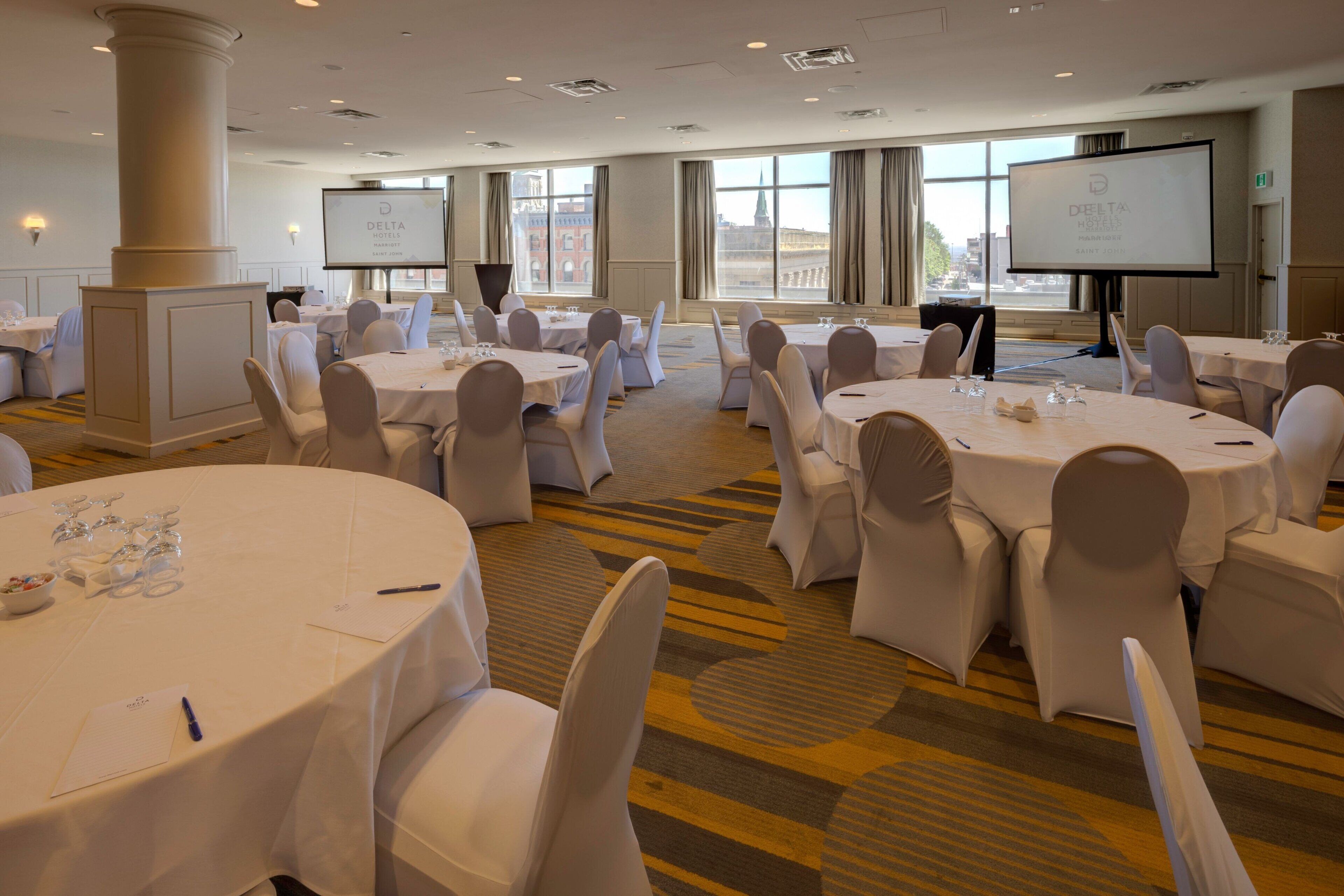 A conference room with multiple round tables, white chairs, and a large screen for presentations.